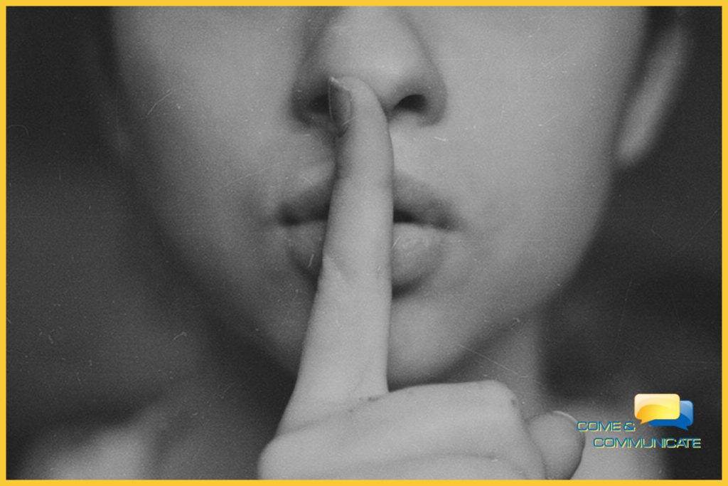 Cara de una mujer con el dedo índice en sus labios para hacer la señal de silencio.