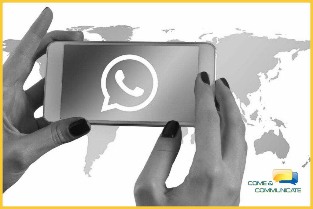 Manos de una mujer sujetando un móvil y un mapamundi de fondo, viendo cómo utilizar WhatsApp para vender.