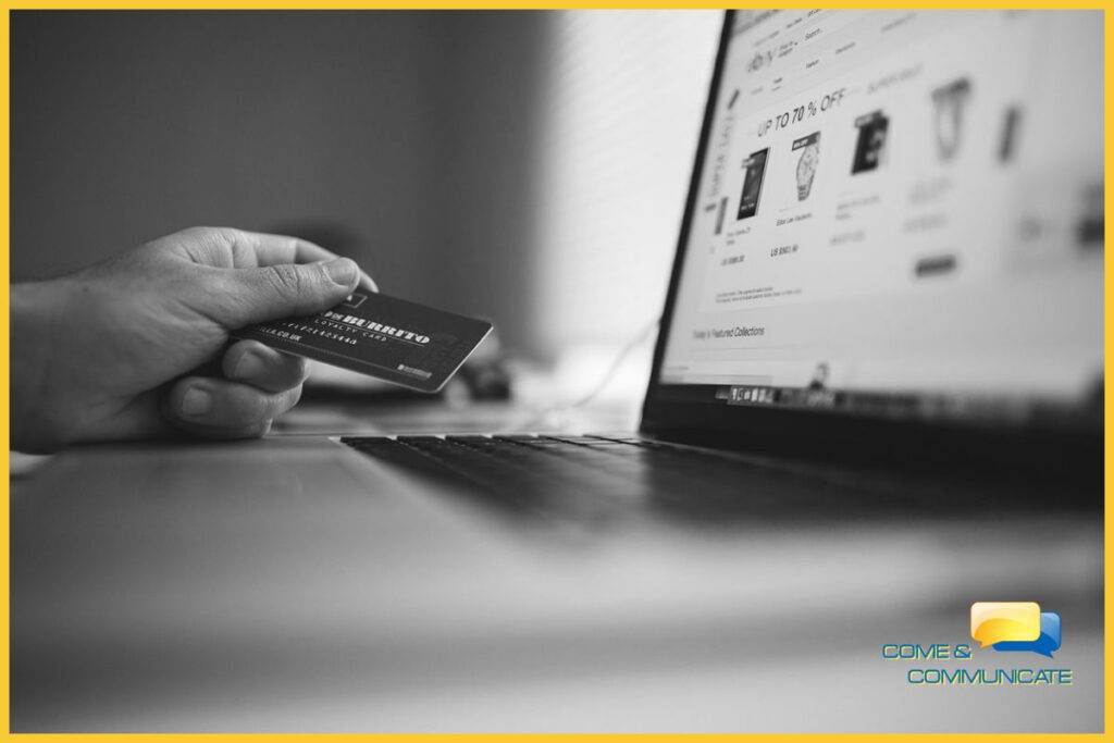 Mano sujetando una tarjeta de crédito con el portátil al lado para realizar una compra online